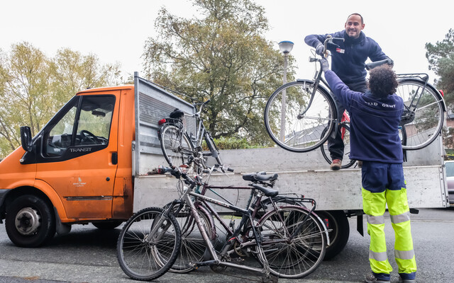 twee medewerkers laden weesfietsen op een bestelwagen